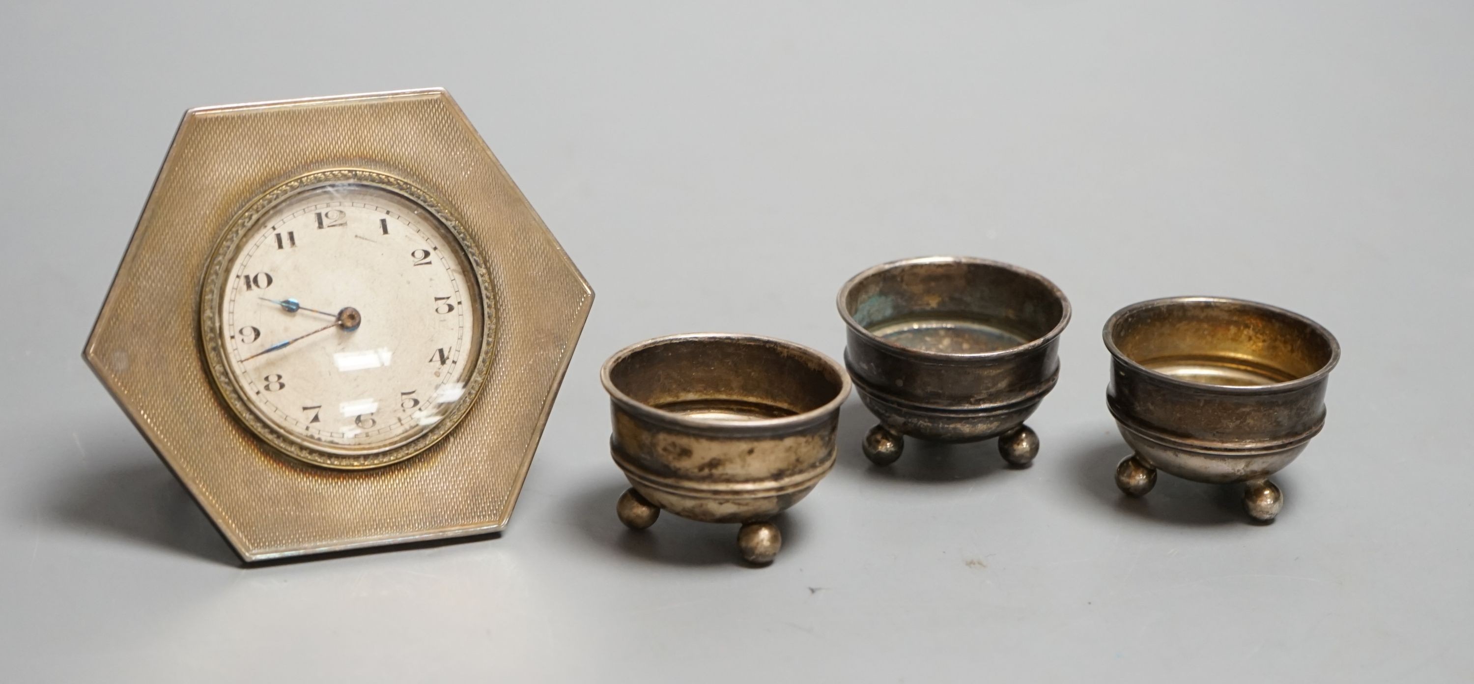 A silver mounted easel strut timepiece and three George V silver salt cellars.